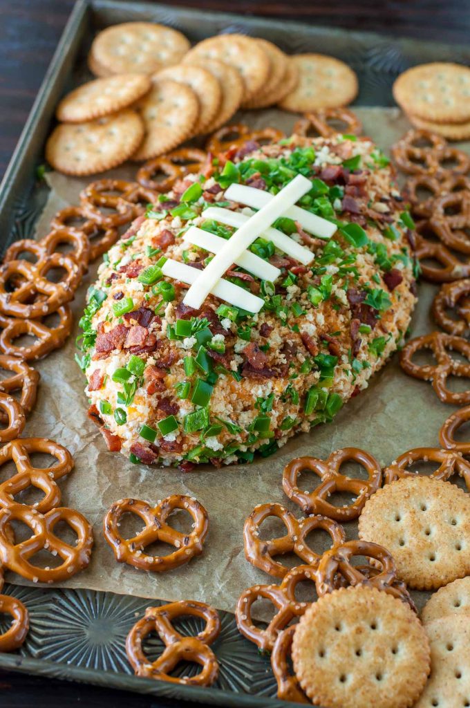 Jalapeño Popper Football Cheese Ball on a sheet pan surrounded by crackers and pretzels for dipping