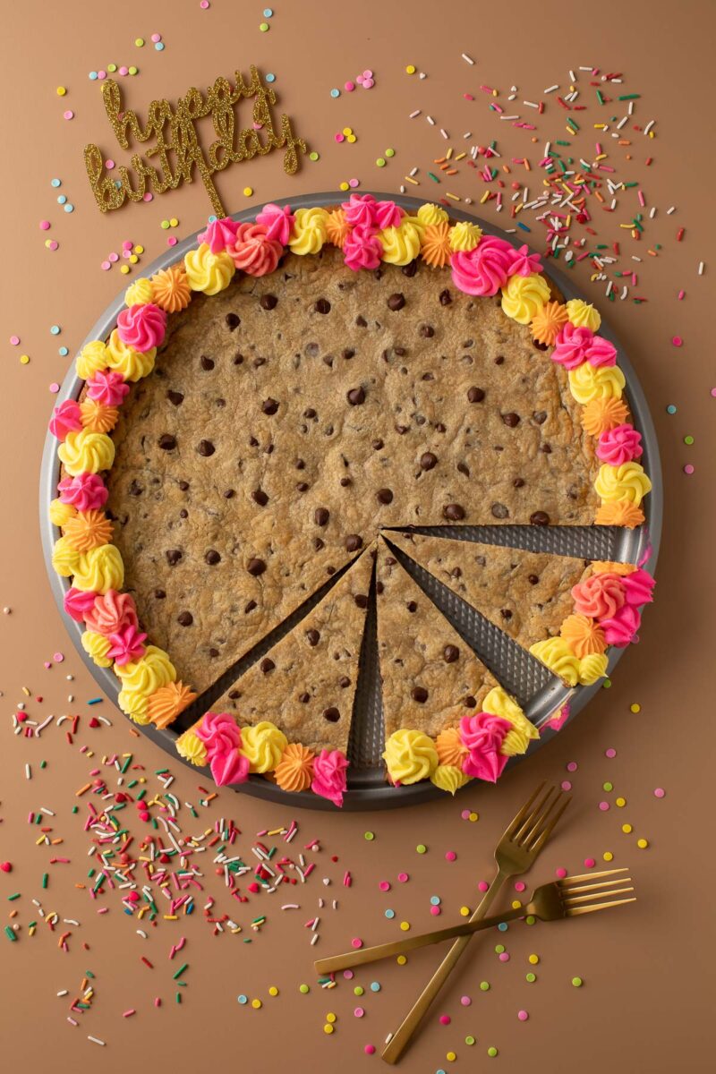 large pizza pan with chocolate chip cookie cake, frosting, and sprinkles