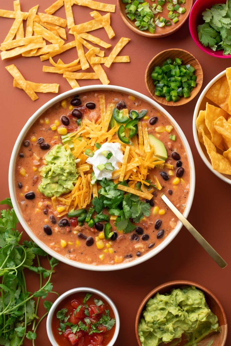 Cheesy Chicken Taco Soup topped with avocado, sour cream, shredded cheese, cilantro, jalapeño, and crispy tortilla strips 