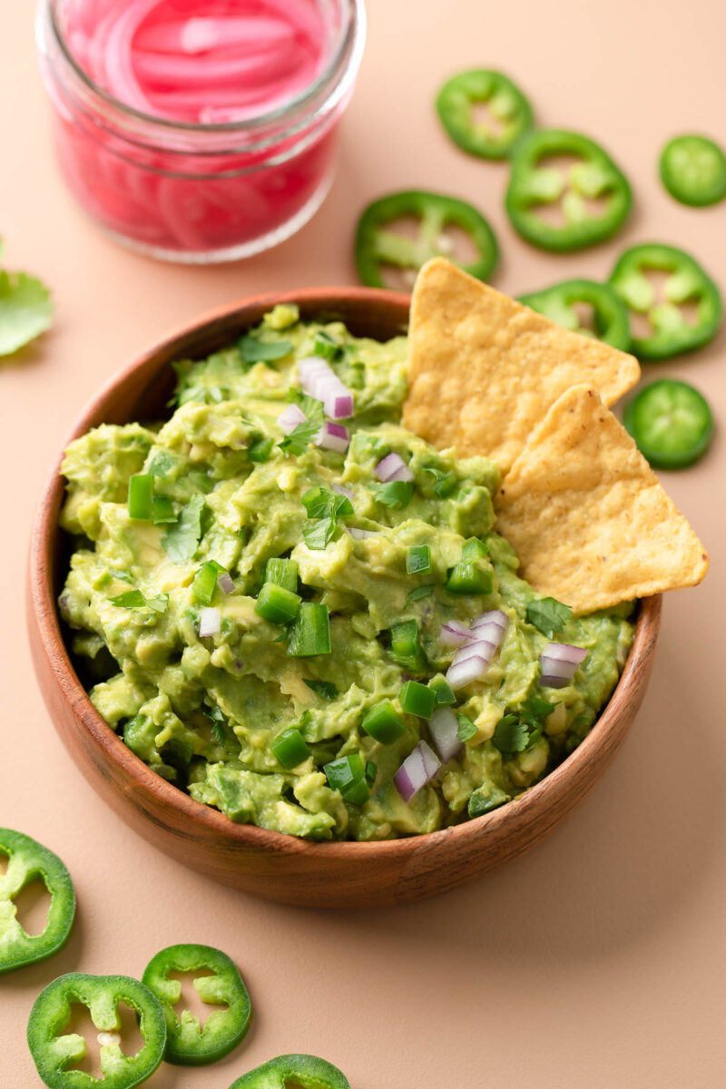 Spicy guacamole in a bowl with jalapeños, red onion, cilantro, lime and tortilla chips on top