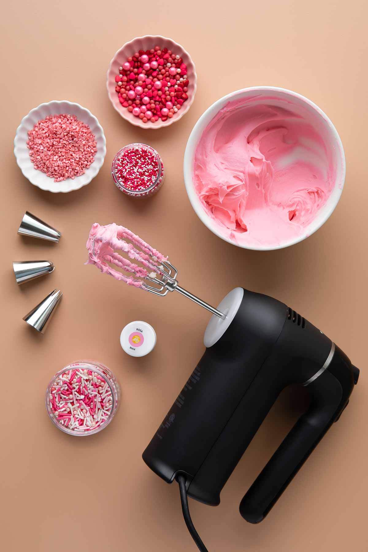 pink frosting with sprinkles, hand mixer, and piping tips