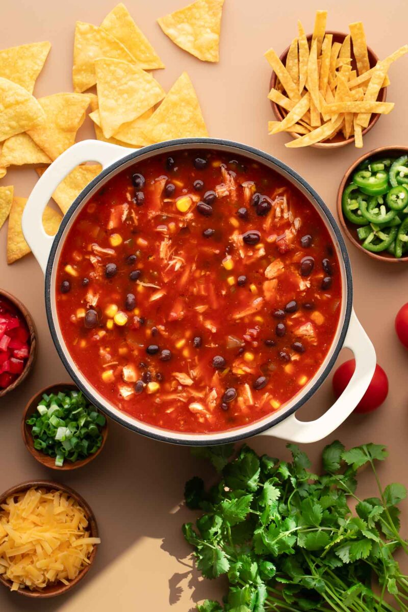 chicken tortilla soup in dutch oven pot surrounded by bowls tortilla soup toppings