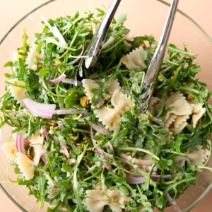 Lemon Pasta Salad topped with pistachio, arugula, parmesan cheese, and red onions