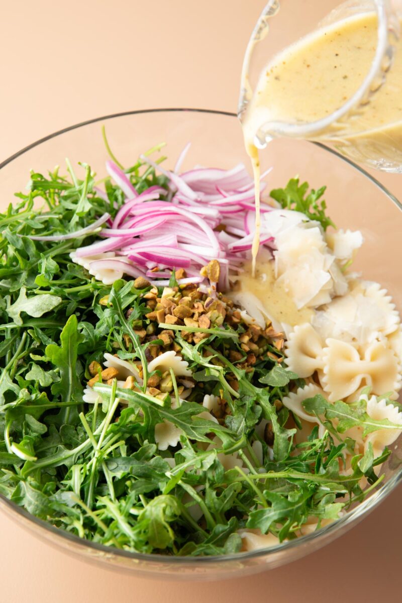 lemon dressing poured over salad ingredients in a mixing bowl