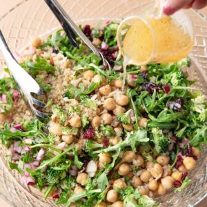 lemon vinaigrette dressing poured over serving bowl of quinoa arugula salad with almonds and dried cranberries