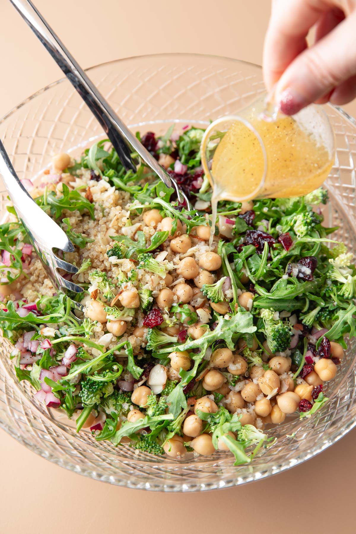 lemon vinaigrette dressing poured over serving bowl of quinoa arugula salad with almonds and dried cranberries