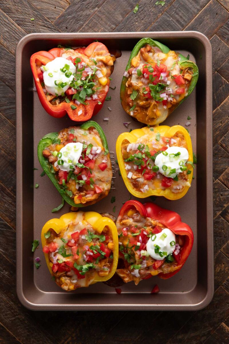 baked Chicken Enchilada Stuffed Peppers topped with cheese, pico de gallo, sour cream, and green onions