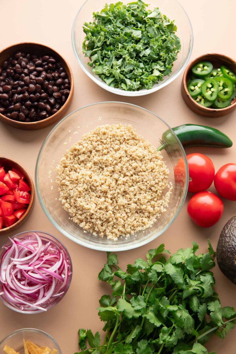 bowls of quinoa, black beans, kale, jalapeno peppers, tomatoes, red onions, tortilla strips, avocado
