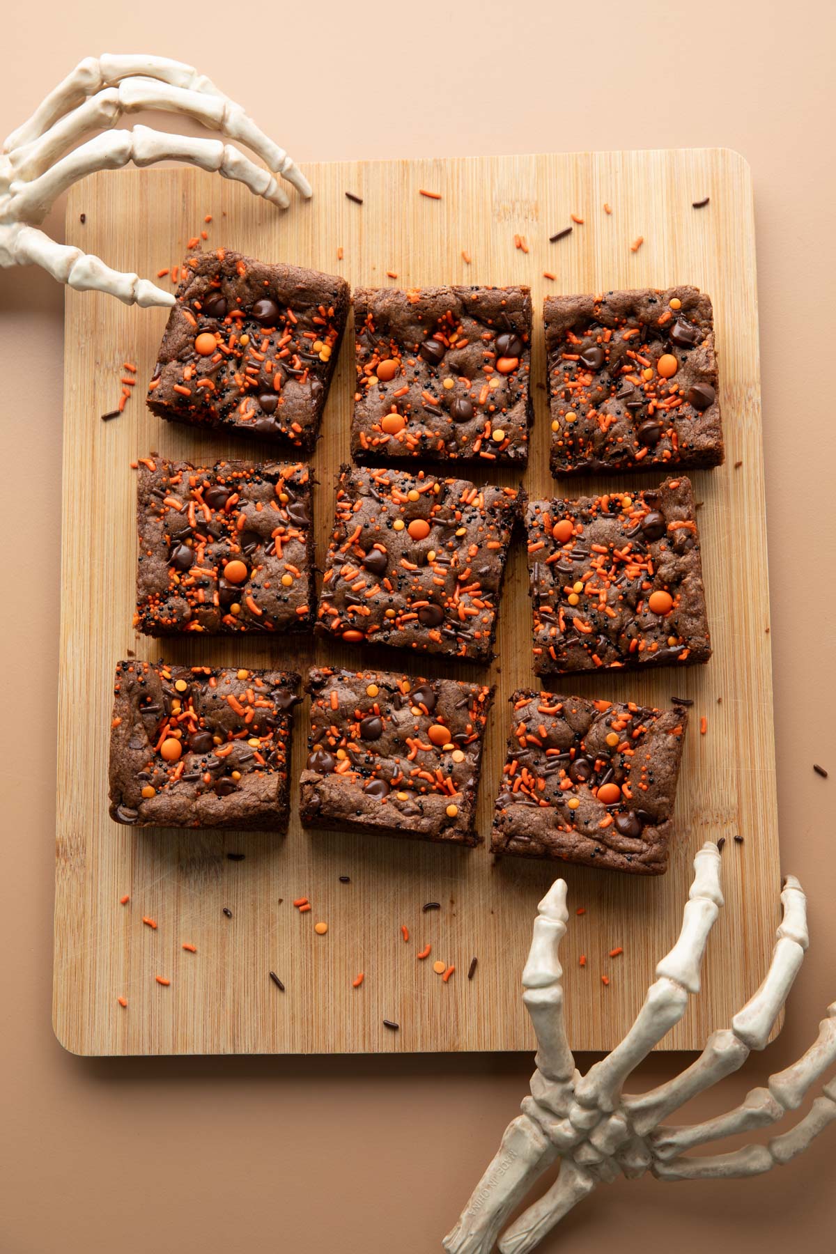 double chocolate cookie bars with halloween sprinkles on a cutting board with skeleton hands